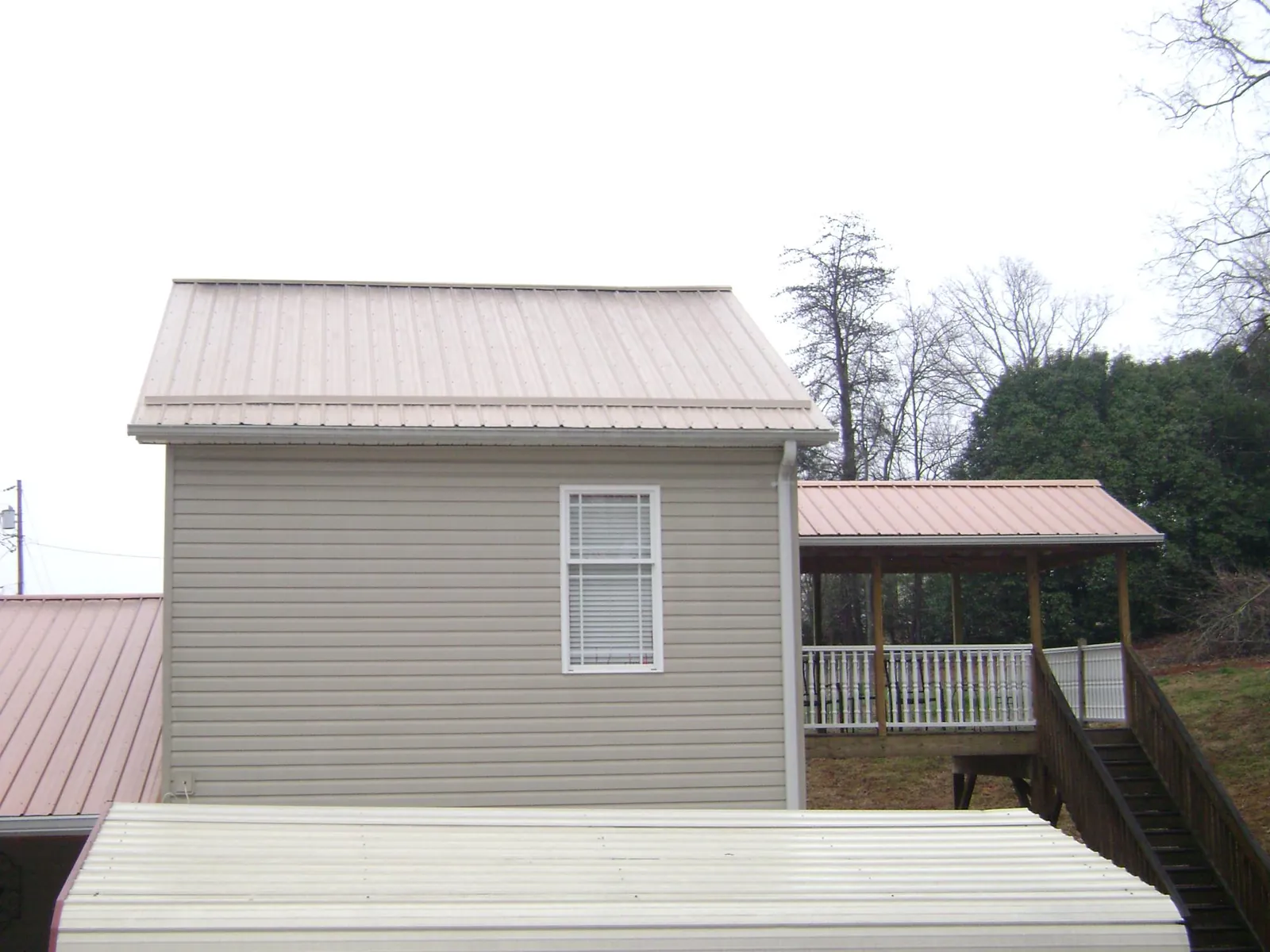 Tan metal roofs on a two story addition and attached porch, from a Roof Replacement job in Beaver